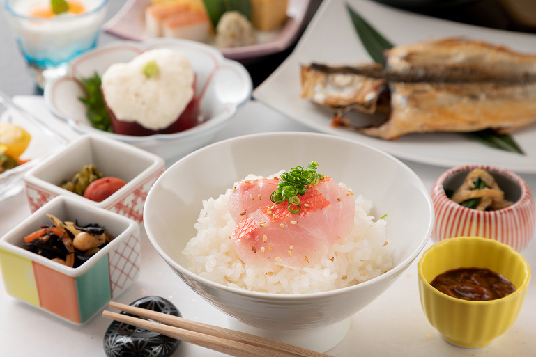 魚の刺身がのった白ご飯、焼き魚、煮物、漬物、デザートなどが並ぶ、上品な日本の朝食膳。