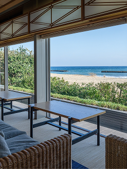 室内から見える、明るい日差しの降り注ぐ砂浜と青い海の風景。
