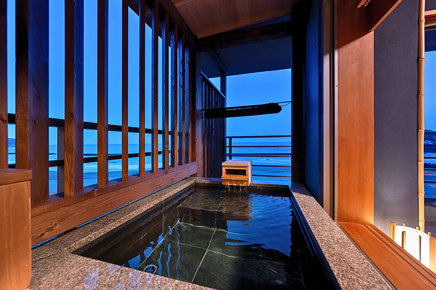 黒いタイル張りのシャワールームと、屋根付きの露天風呂が隣接する浴室。