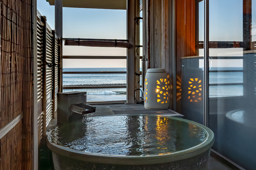 深い藍色の夜の海を見渡せる客室。低いベッドが二つ並び、白いシーツがかけられている。ベッドの足元は一段高くなった木製の床で、その先は畳敷きになっている。