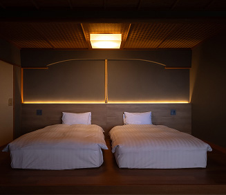 夜の静けさに包まれた、落ち着いた雰囲気の寝室。一段高くなった木製の床の上に、白い清潔な布団が二つ並んでいます。